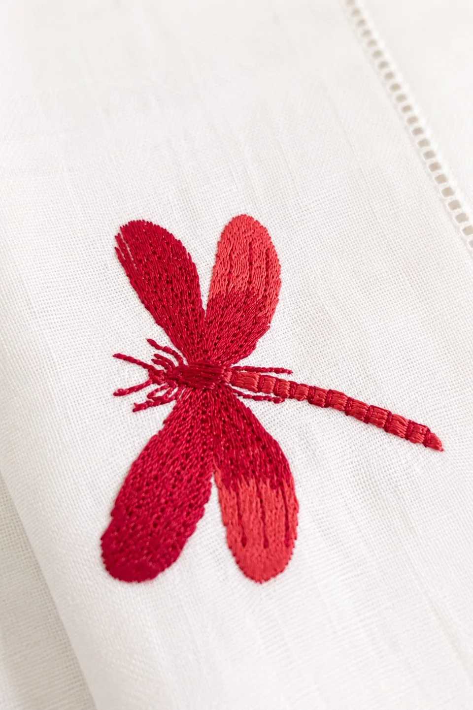 Detalle del bordado a mano de una libélula roja sobre lino, con vainica en el remate
