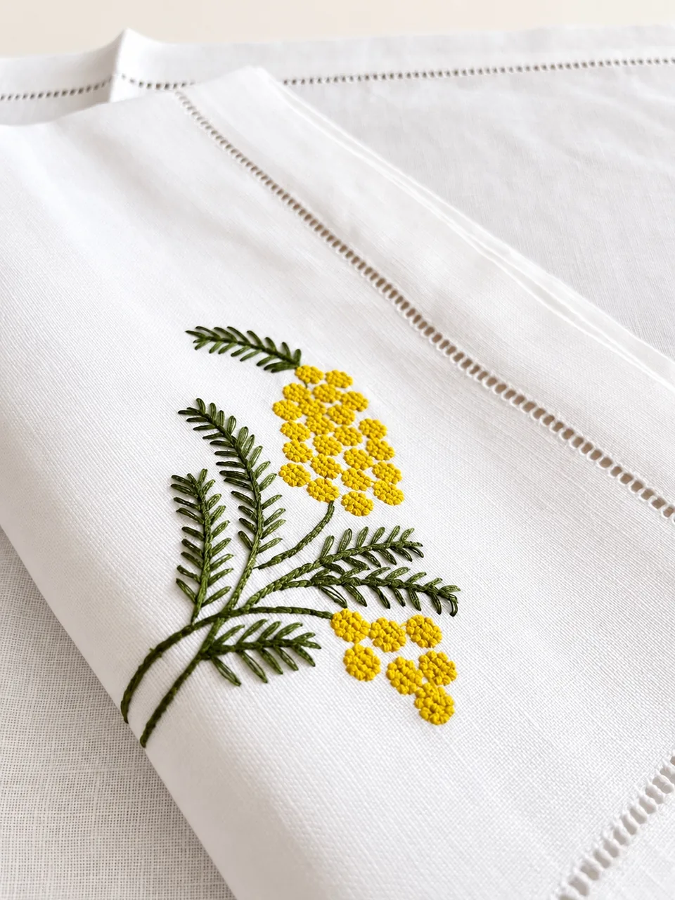 Detalle del bordado de mimosa, con sus flores amarillas en relieve y las hojas verdes, junto a la vainica