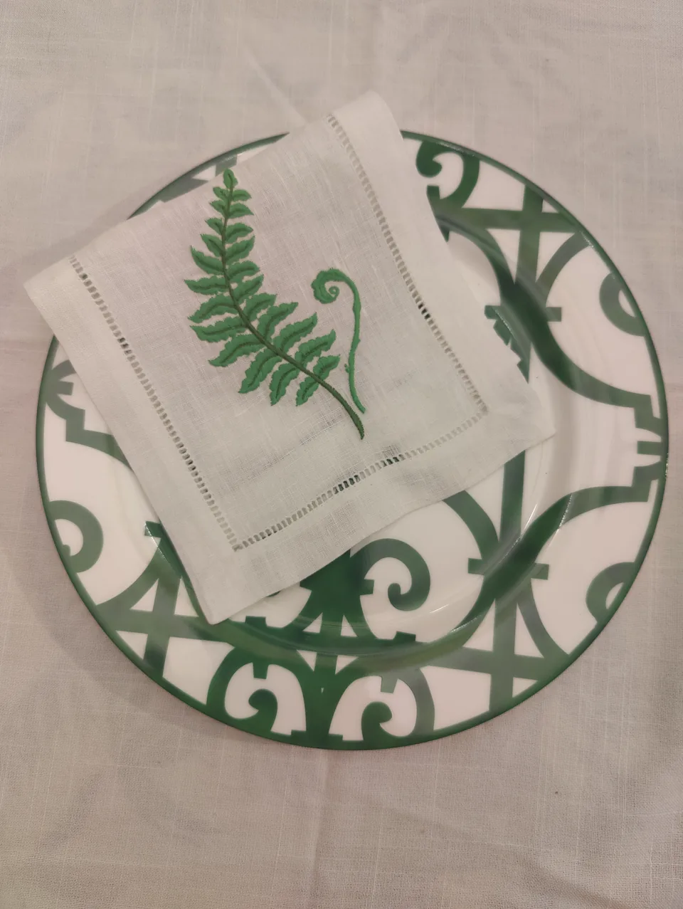 Servilleta de cóctel de helecho doblada sobre un bajo plato de Rejas verde